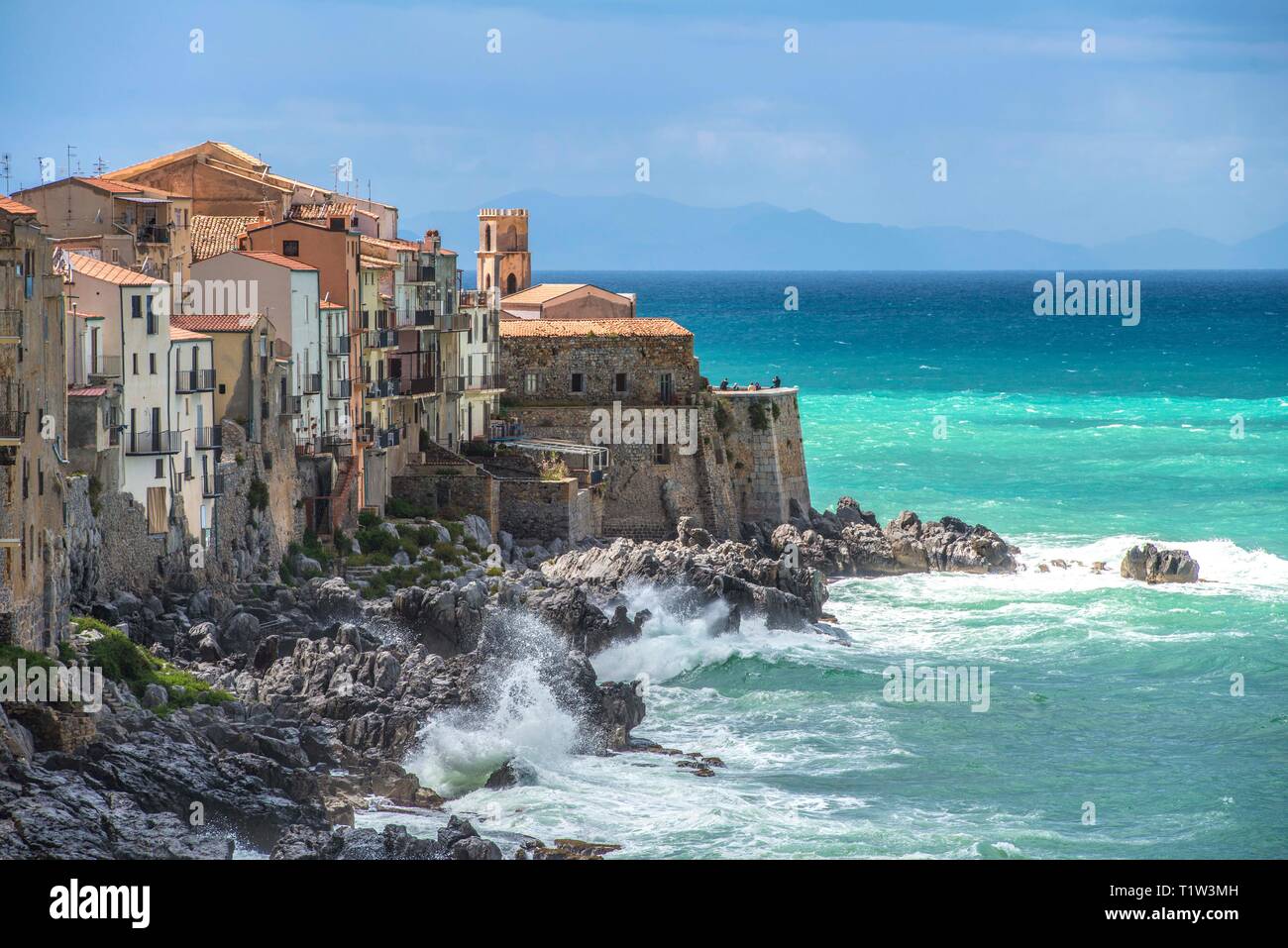 L'Italia, sicilia, di onde che si infrangono contro la costa della pittoresca città di Cefalù. La Chiesa dell'Itria domina il punto nord Foto Stock