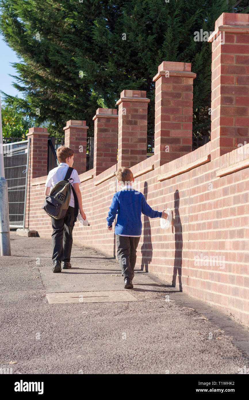 Due giovani scolari a casa a piedi lungo una tranquilla UK strada residenziale Foto Stock