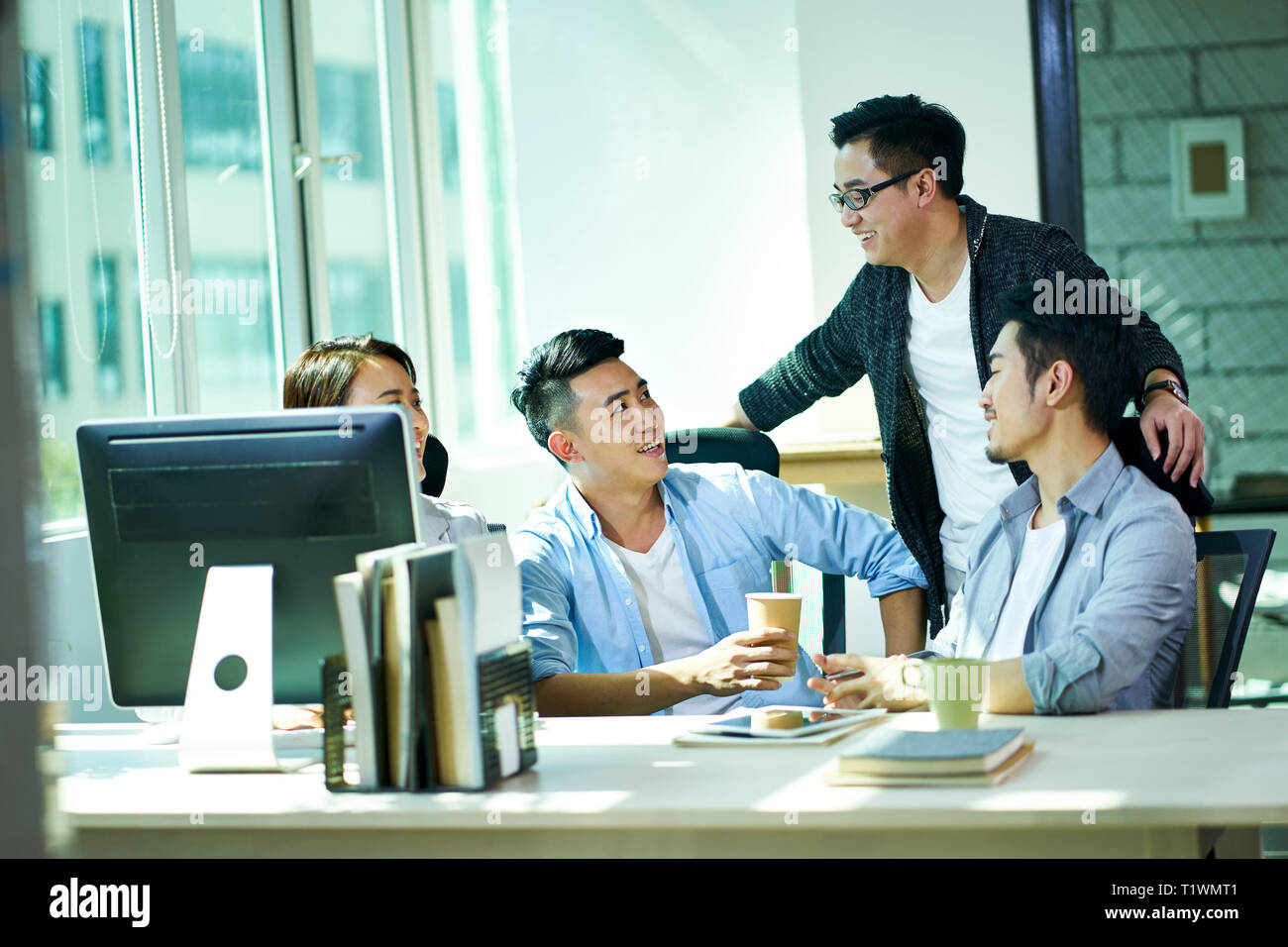 Quattro giovani uomini d'affari asiatici conversare in ufficio, felici e rilassati. Foto Stock