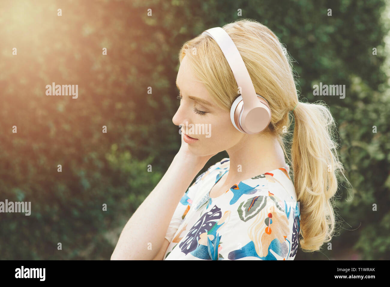 Vista della giovane donna caucasica ascoltare musica ed essendo ispirata in un ambiente esterno Foto Stock