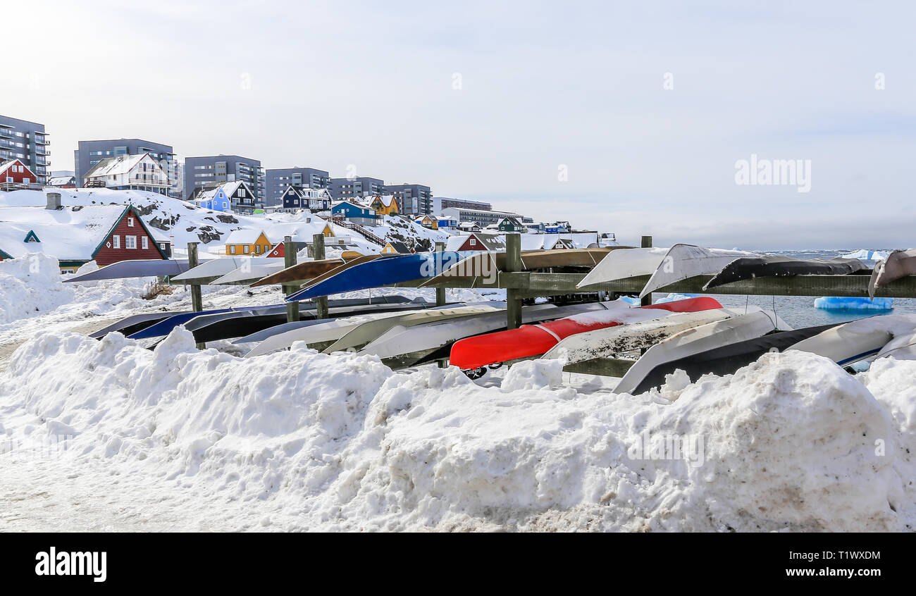 Kayaks Inuit memorizzati per un tempo in inverno la neve con gli edifici moderni e piccoli cottage in background, Nuuk città vecchia porto, Groenlandia8 Foto Stock