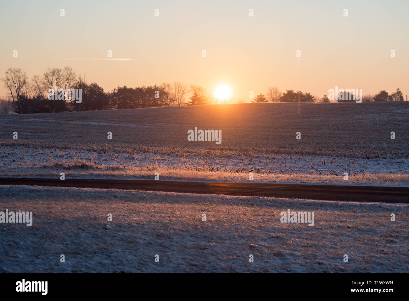 Un profondo orange sunrise brilla attraverso un campo e attraverso una strada Foto Stock