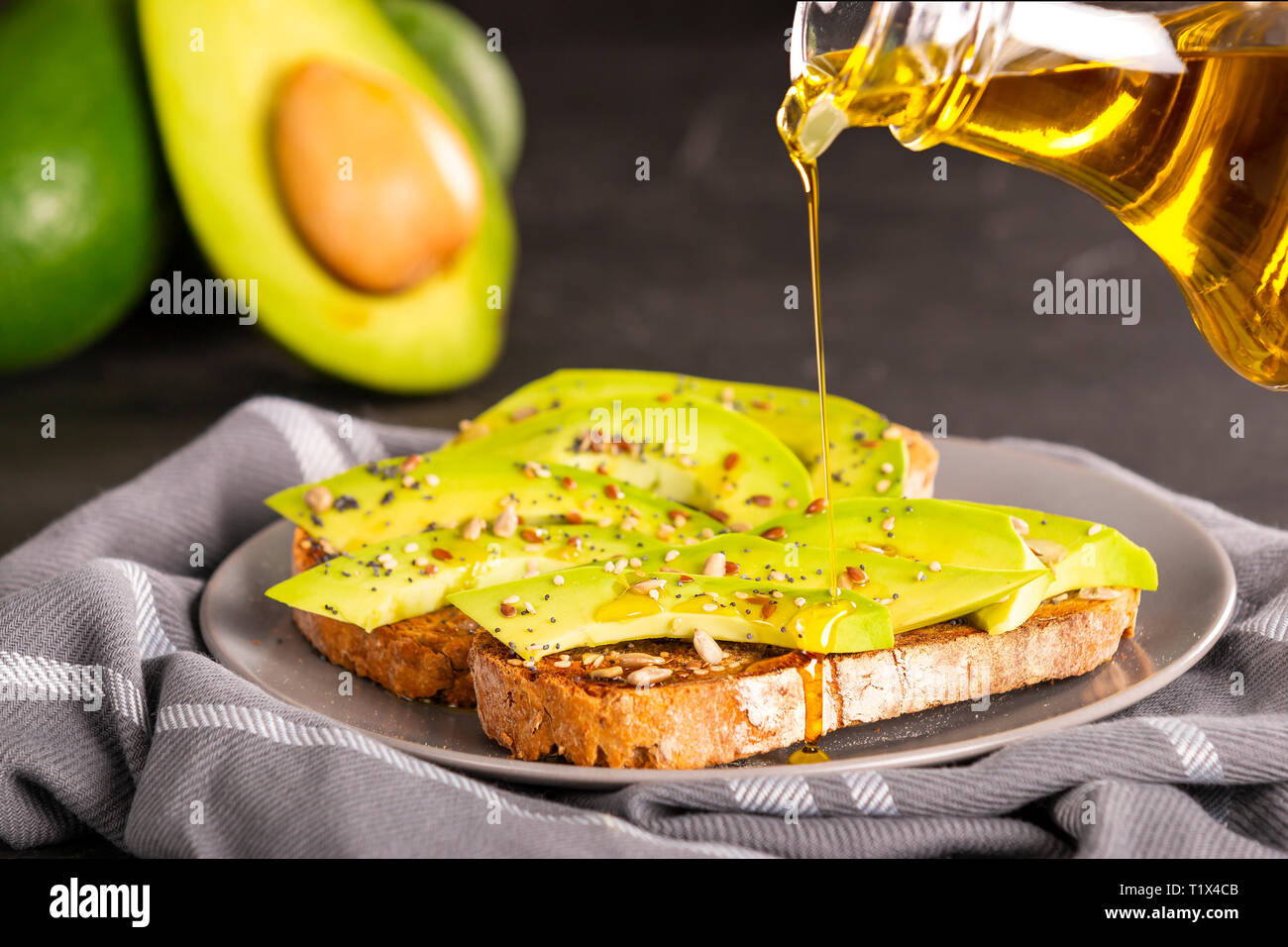 Olio fresco riversando gustosi panini con fettine di avocado e spezie Foto Stock