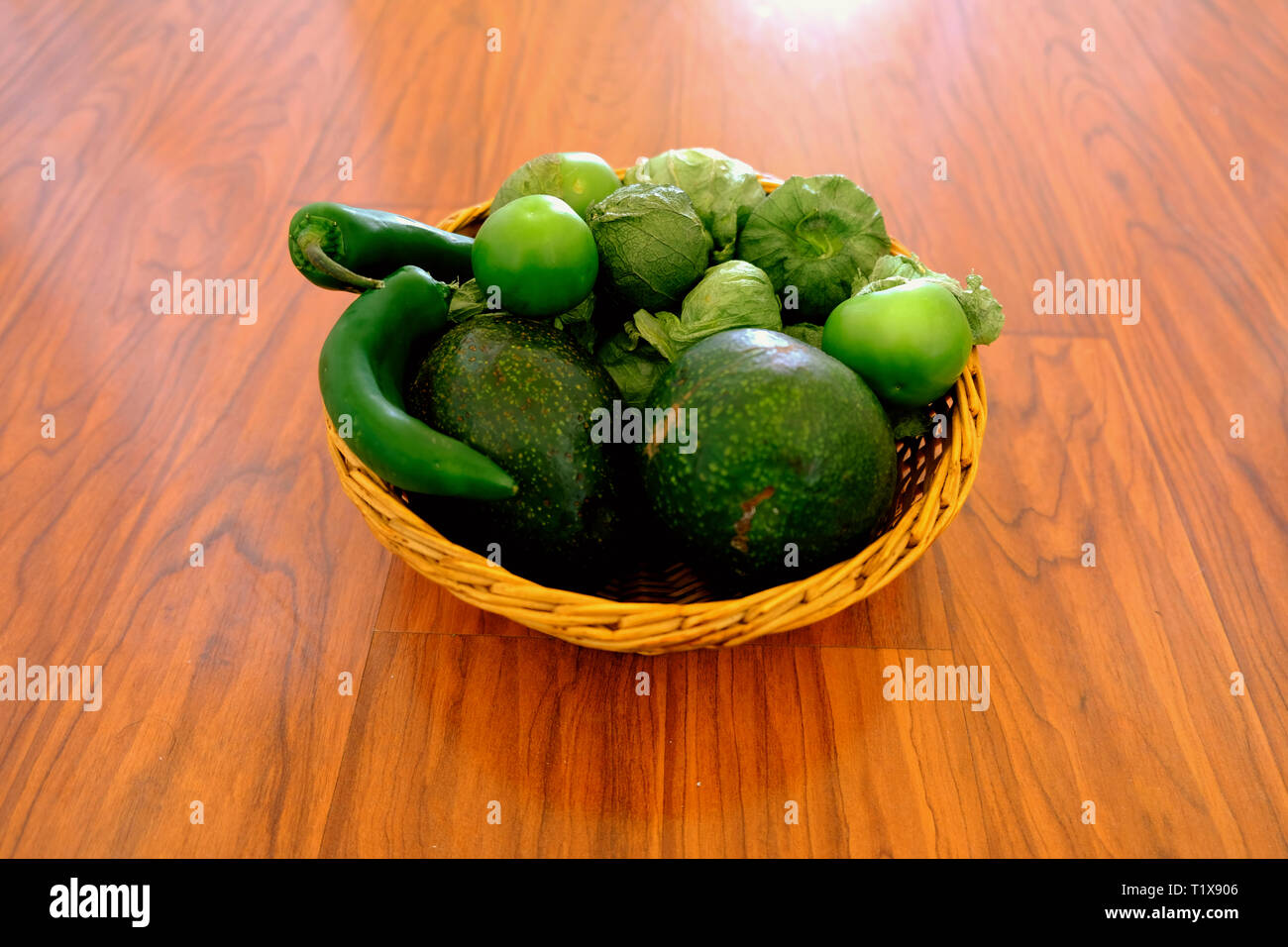 Ingredienti per la salsa di avocado in un cesto tessuto su una superficie in legno: avocado, tomatillos, jalapeños. Foto Stock