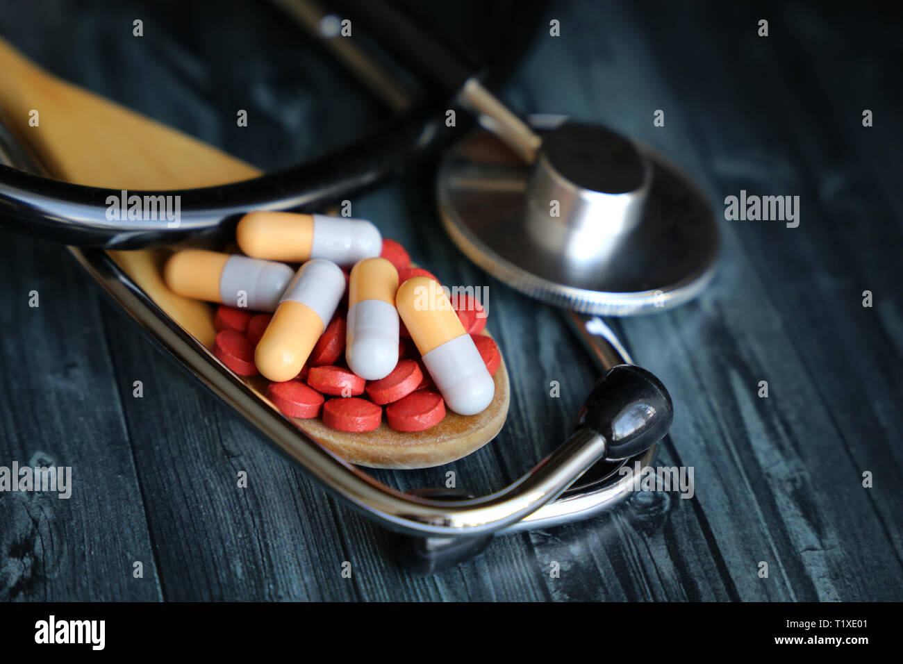 Assistenza sanitaria e farmacia, pillole e capsule in un cucchiaio di legno e stetoscopio scuro su un tavolo di legno. Concetto di farmaci, vitamine, cardiologia, trattamento Foto Stock
