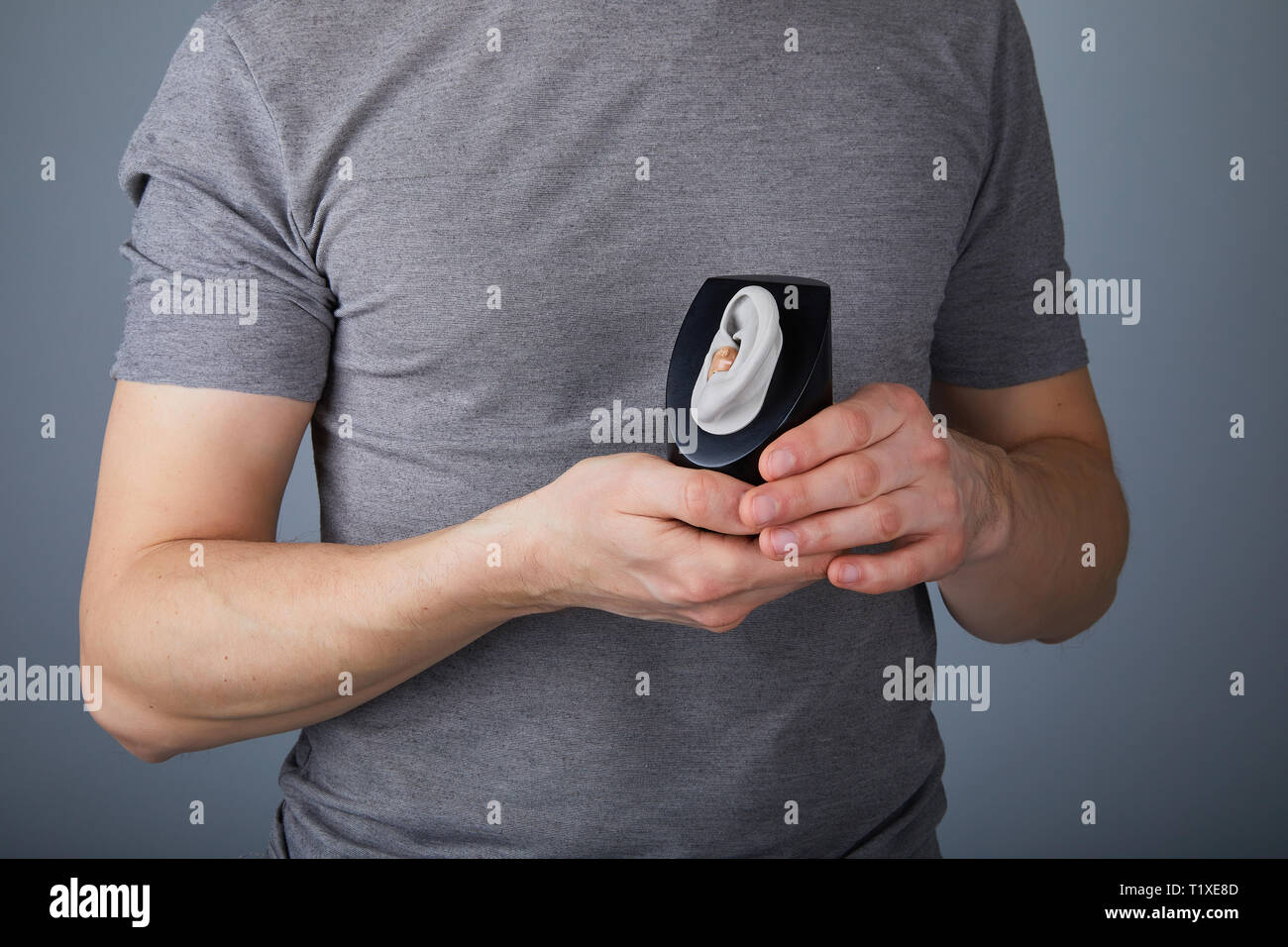 Uomo che mostra l'uso di apparecchi acustici, closeup. Apparecchi acustici su sfondo grigio, alternativa alla chirurgia. Foto Stock