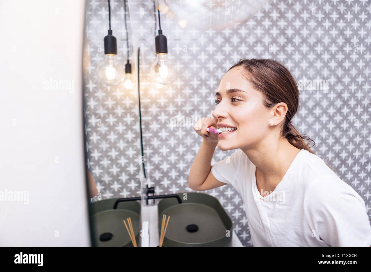 Dai capelli scuri donna spazzolatura dei denti nella sua luce bagno moderno Foto Stock