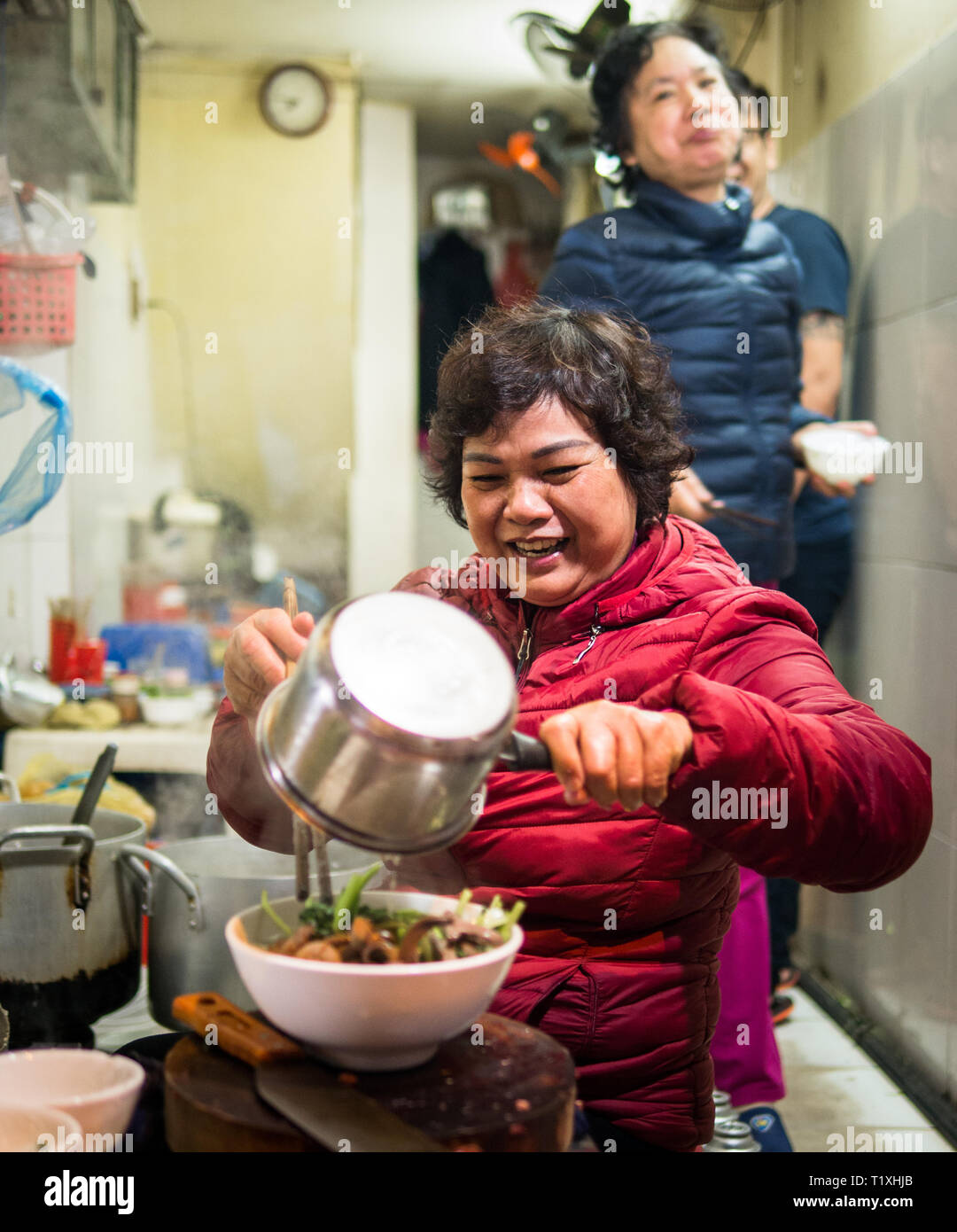 Donna vietnamita la preparazione di cibo di strada con la sua famiglia in un piccolo negozio di mercato, Hanoi, Vietnam Foto Stock