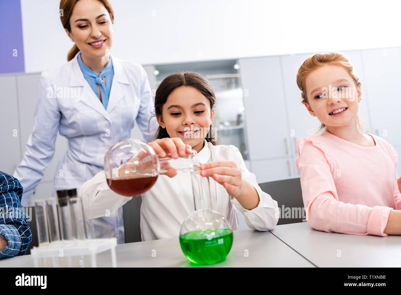 La scolaretta sorridente con bicchieri facendo esperimento chimico durante la lezione di Chimica Foto Stock