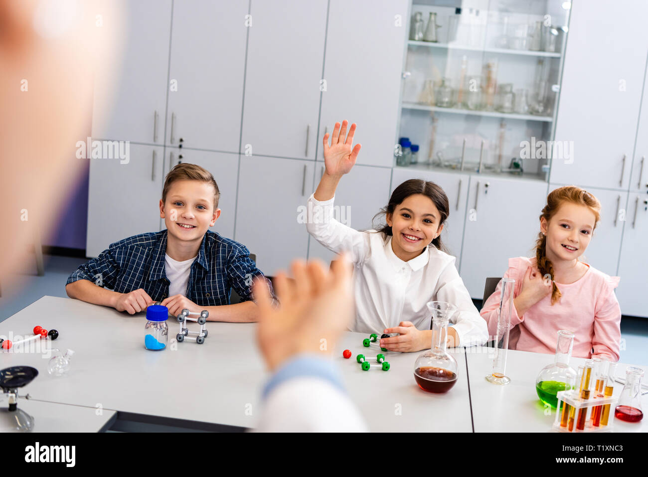 Sorridente schoolgirl alzando la mano in classe durante la lezione di Chimica Foto Stock