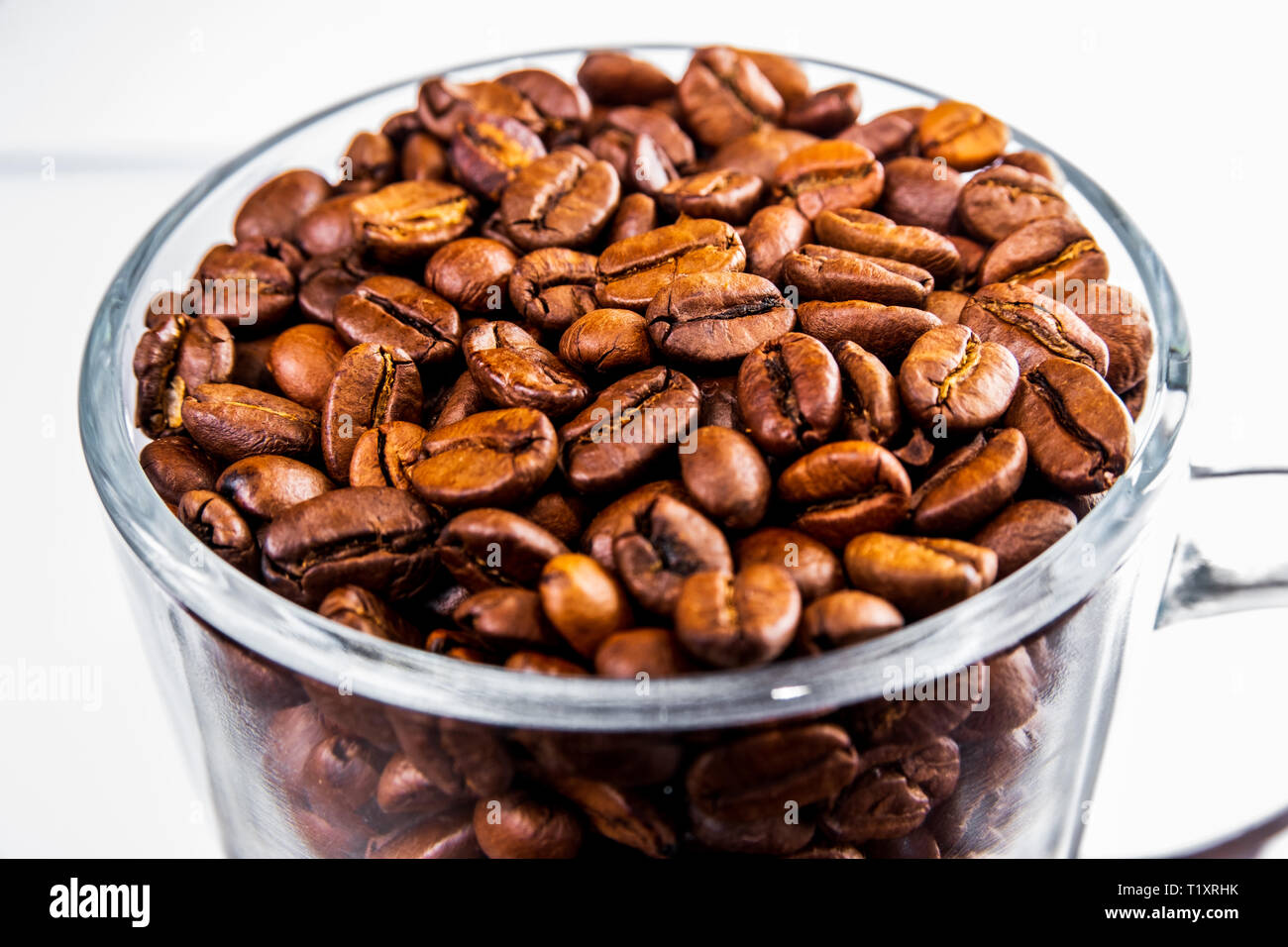 Chicchi di caffè tostati in un bicchiere di vetro isolato su uno sfondo bianco Foto Stock