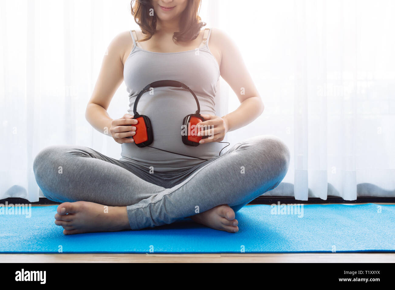 Giovane donna incinta lasciando che il bambino nel ventre di ascoltare la musica al di sopra della finestra vista in mattinata con spazio di copia Foto Stock