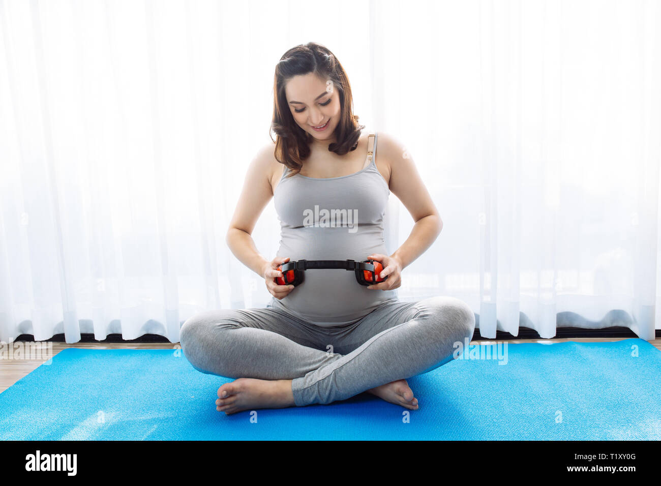 Attraente giovane donna incinta lasciando che il bambino nel ventre di ascoltare la musica al di sopra della finestra vista in mattinata con spazio di copia Foto Stock