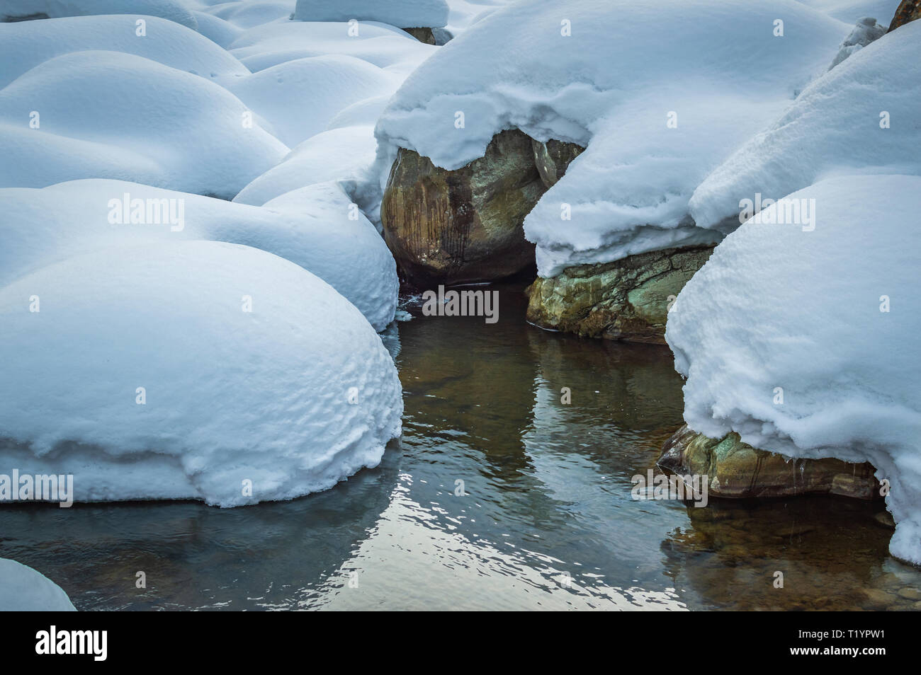 Coperta di neve di massi che racchiude una piccola piscina di acqua durante il periodo invernale in Kashmir Foto Stock