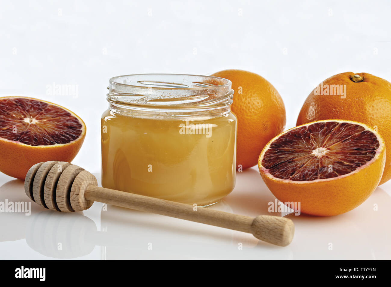 Miele all'arancio in vaso con arance tagliate. primo piano con cucchiaio Foto Stock