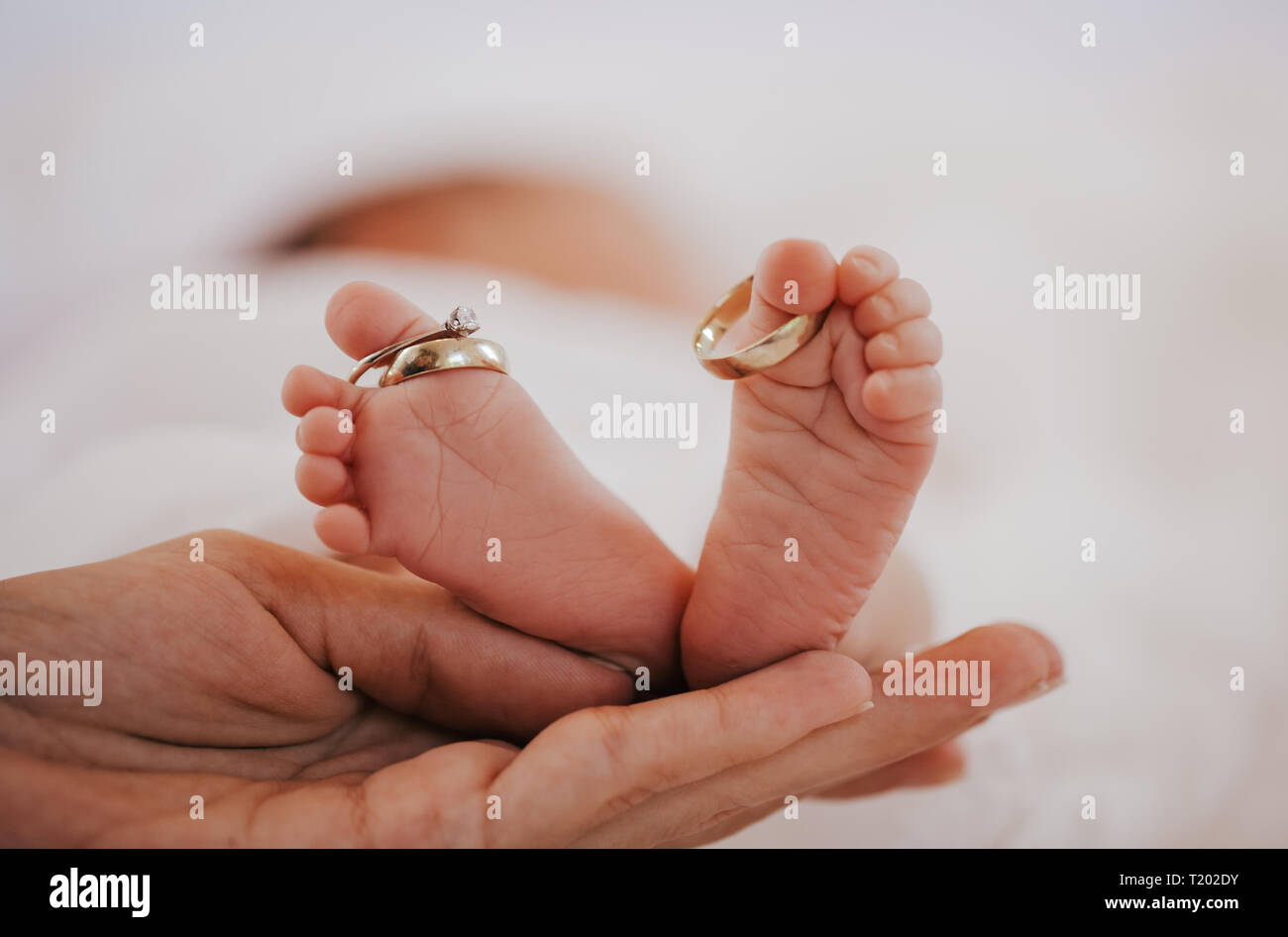 Close up piedi del bambino con gli anelli di nozze su grandi dita. Madre mano tenere i piedi. Foto Stock