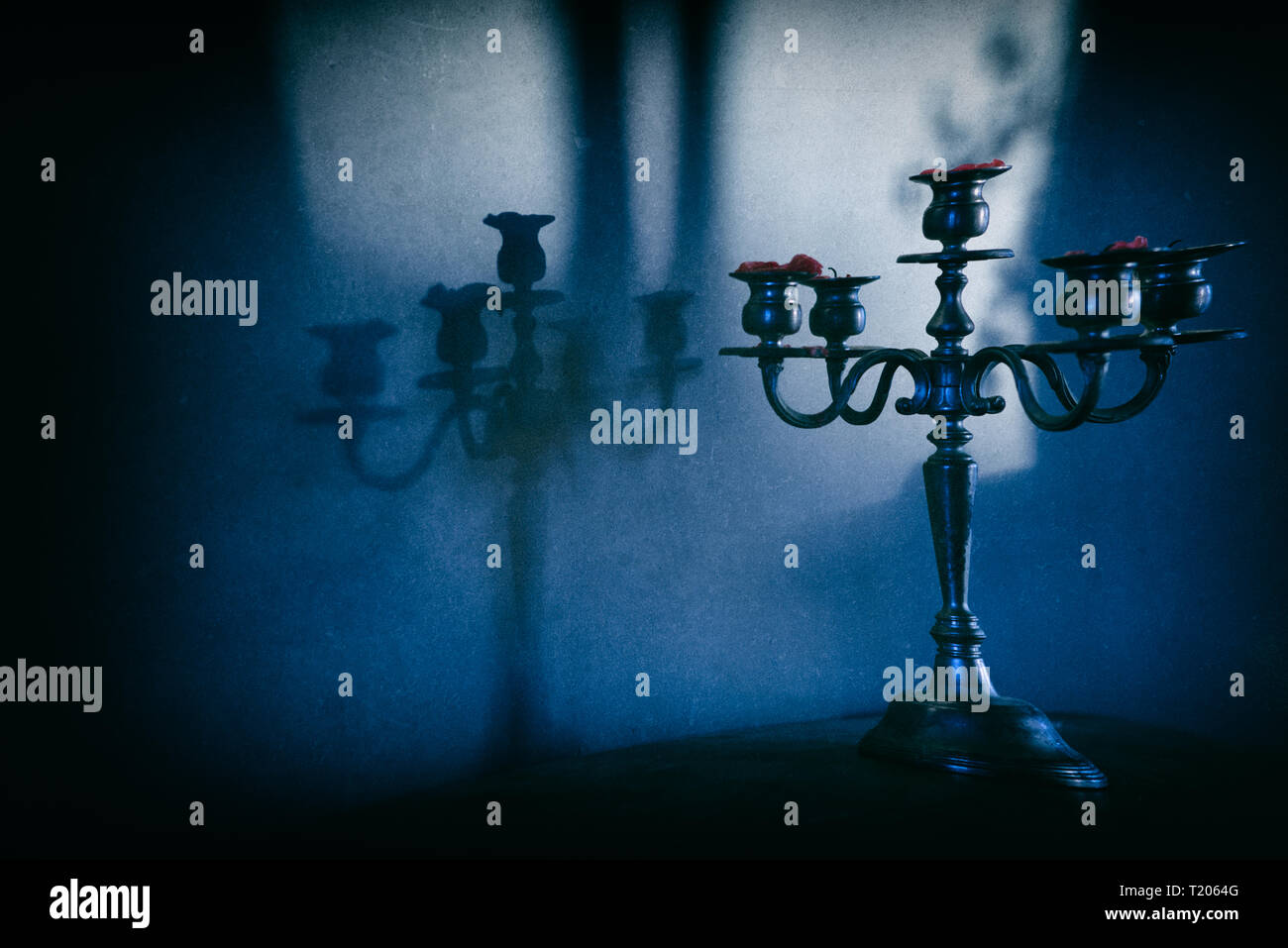 Moody moonlight immagine di ornati candelabri getta un' ombra sulla parete dietro. Le candele rosse vengono bruciate. Misteriosa immagine granulosa. Foto Stock