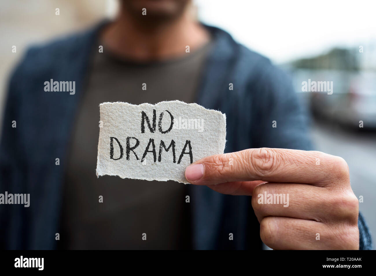 Primo piano di un giovane uomo caucasico sulla strada, indossare abiti casual, che mostra un pezzo di carta con il testo no drama scritto in esso Foto Stock
