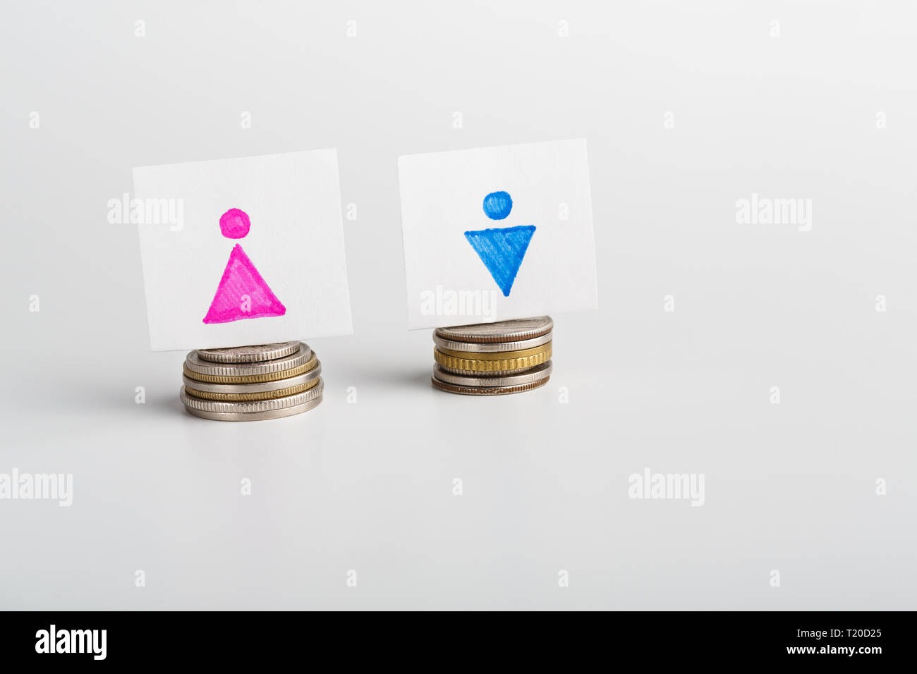 Parità di retribuzione per uomo e donna, le carte con le figure di genere e simili di pile di monete, sfondo bianco con spazio vuoto Foto Stock