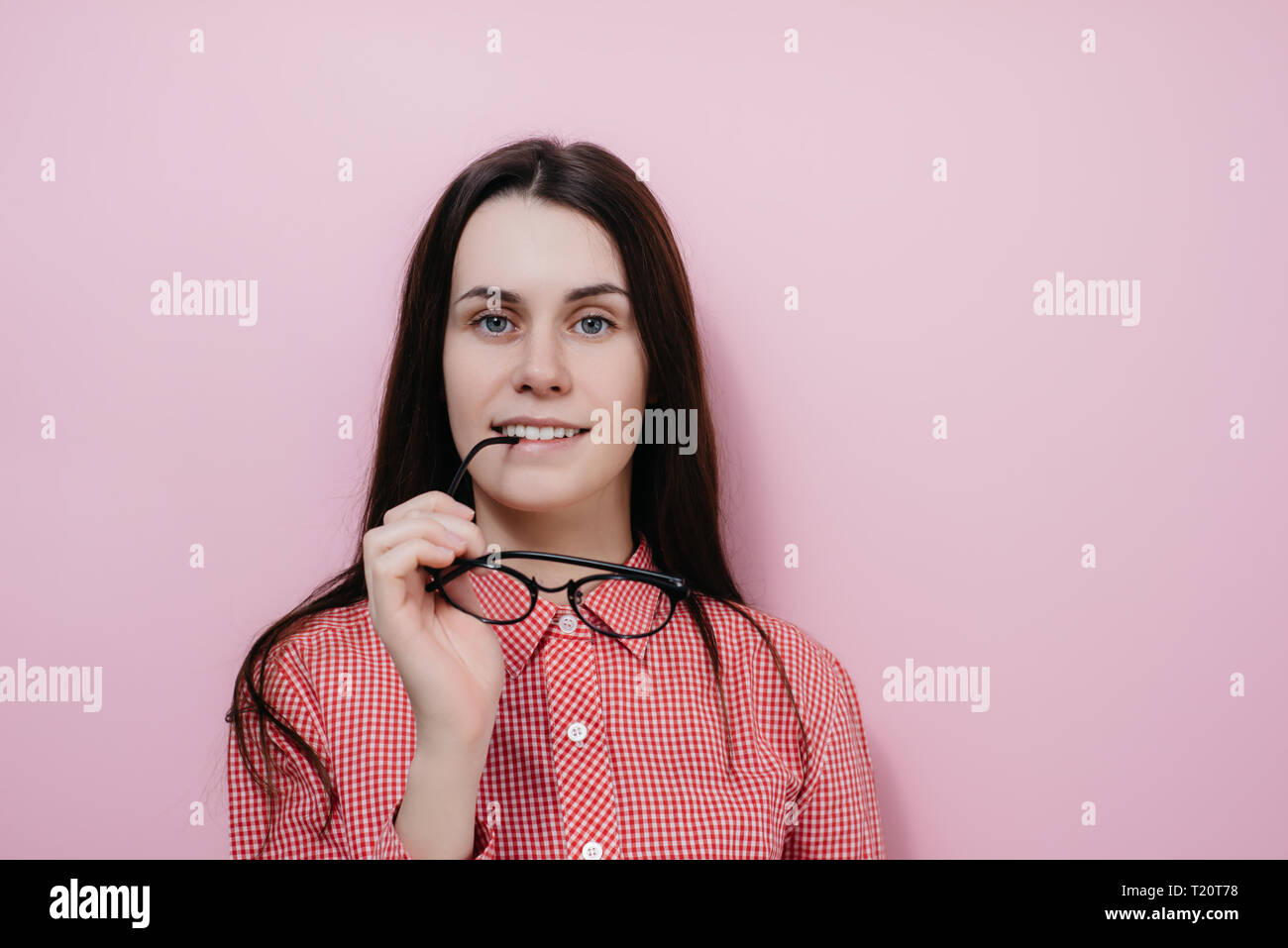 Ritratto di felice giovane donna mantiene i bicchieri in prossimità delle labbra, gioisce ricezione di complimento, vestito in abiti casual, isolate su sfondo rosa Foto Stock