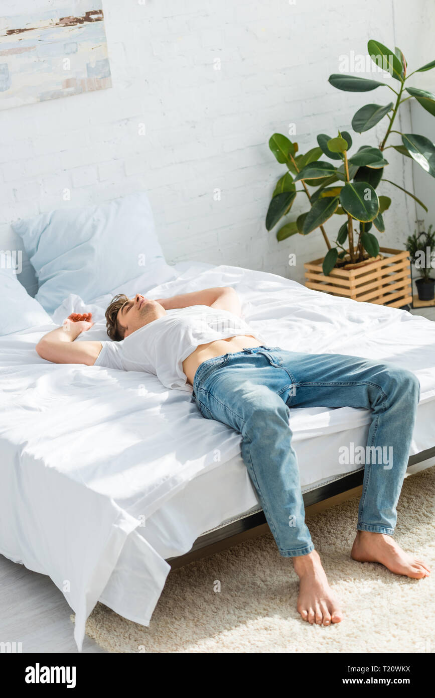 Uomo in maglietta e jeans giacente sul retro sul letto in camera da letto Foto Stock