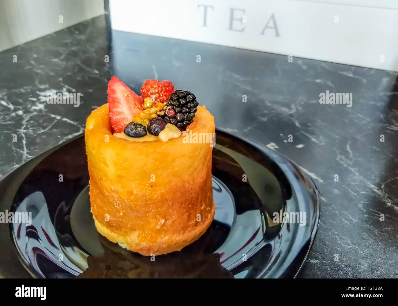 Mini torta decorata con un fresco e fragola, lampone, mora, polvere d'oro, e l'estate bacche sulla tavola nera e piastra nera con tè bianco box. B Foto Stock