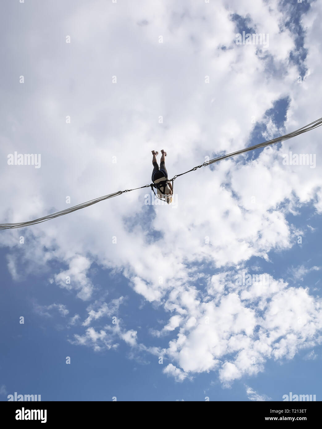 Ragazza appesa in slingshot contro blu cielo nuvoloso. Catapulta ed entusiasmante attrazione in azione. Ragazza godendo della sua fionda amusement ride ad alta saltato a WH Foto Stock