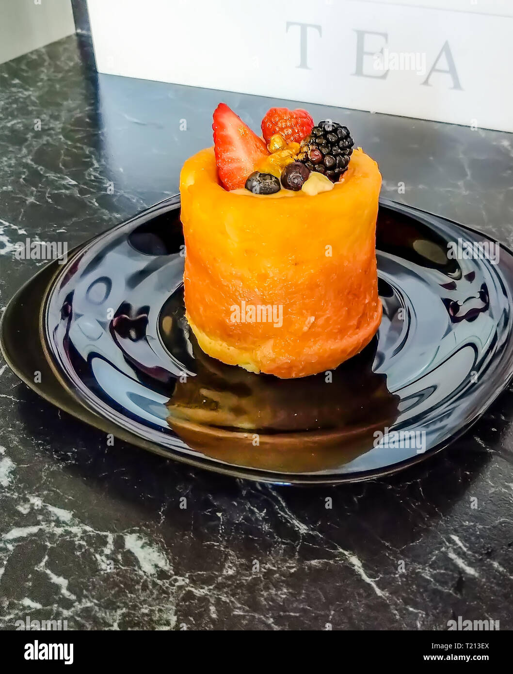 Mini torta decorata con un fresco e fragola, lampone, mora, polvere d'oro, e l'estate bacche sulla tavola nera e piastra nera con tè bianco box. B Foto Stock