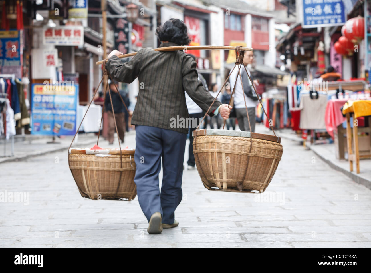 Uomo con polo sulla spalla con due cestelli appesi porta oggetti Market street in un tradizionale vecchio modo Foto Stock