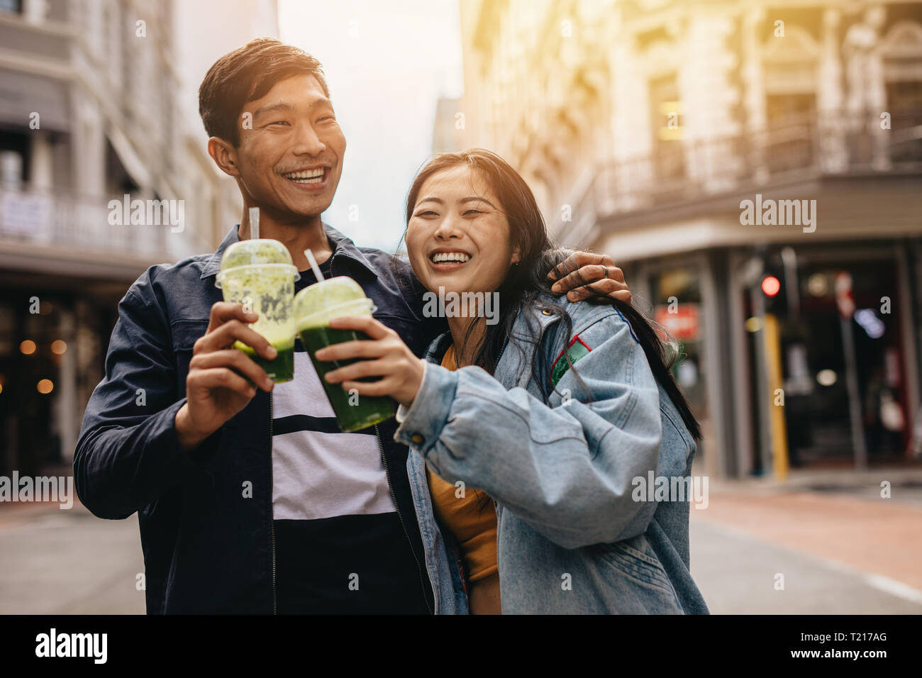 Giovani asiatici giovane camminando sulla strada di città e aver frullato. Felice giovane uomo e donna che cammina sulla strada di città e succo di tostatura. Foto Stock