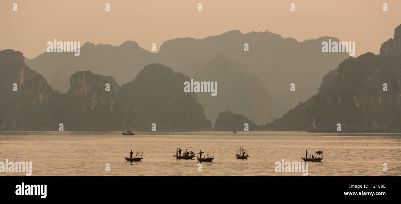 Arancione tramonto colori l'atmosfera come il giorno svanisce nella baia di Halong e barche da pesca legare a ormeggi Foto Stock