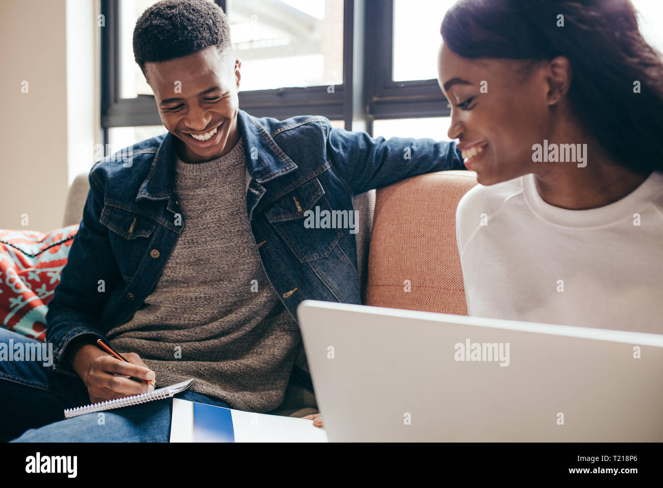 Ragazza africana libro di lettura con il suo compagno di classe rendendo note seduto sul divano di college. Due giovani che completano la loro assegnazione classe all'interno di un campo Foto Stock