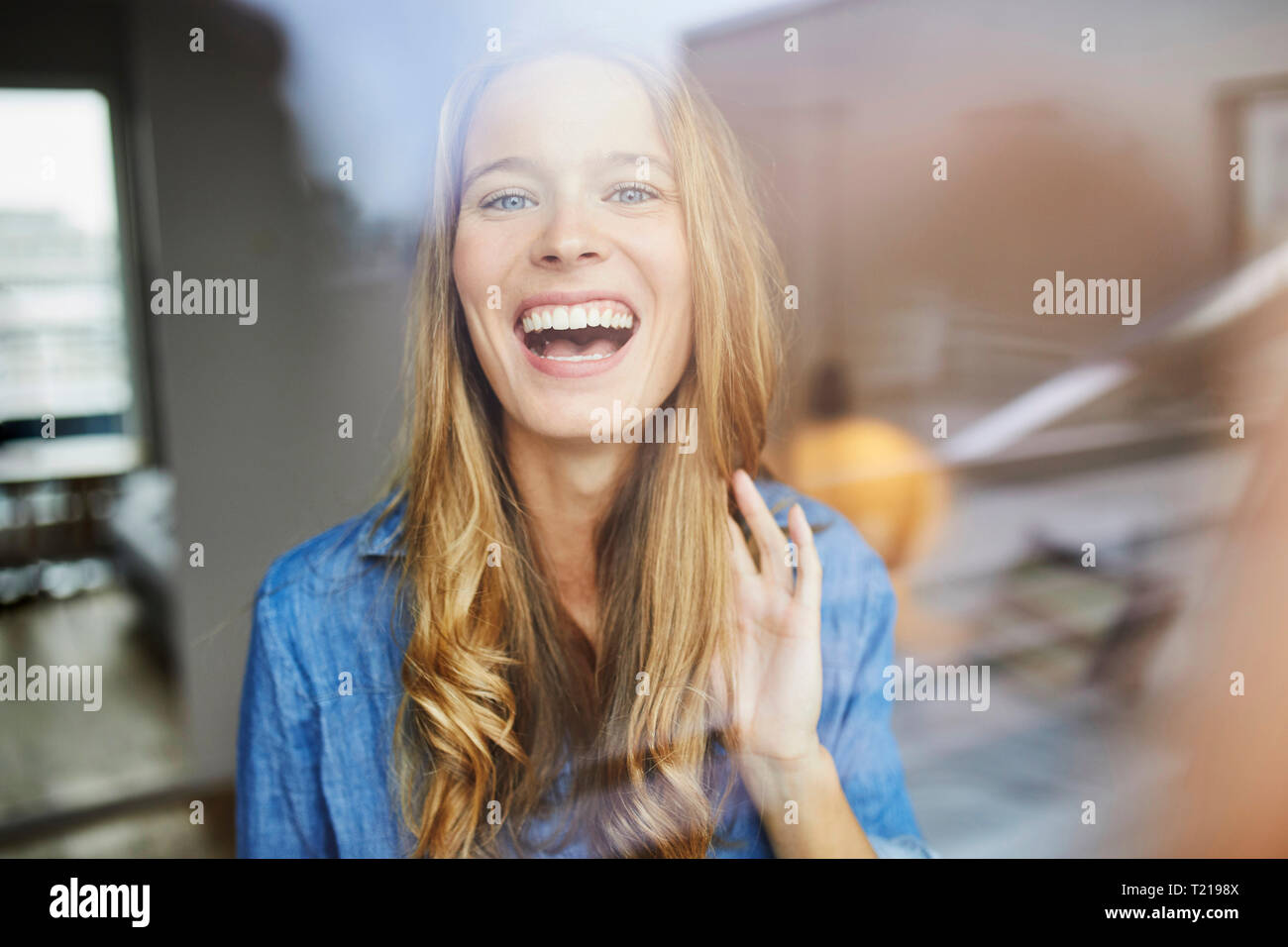 Ritratto di ridere giovane donna dietro il vetro di finestra Foto Stock