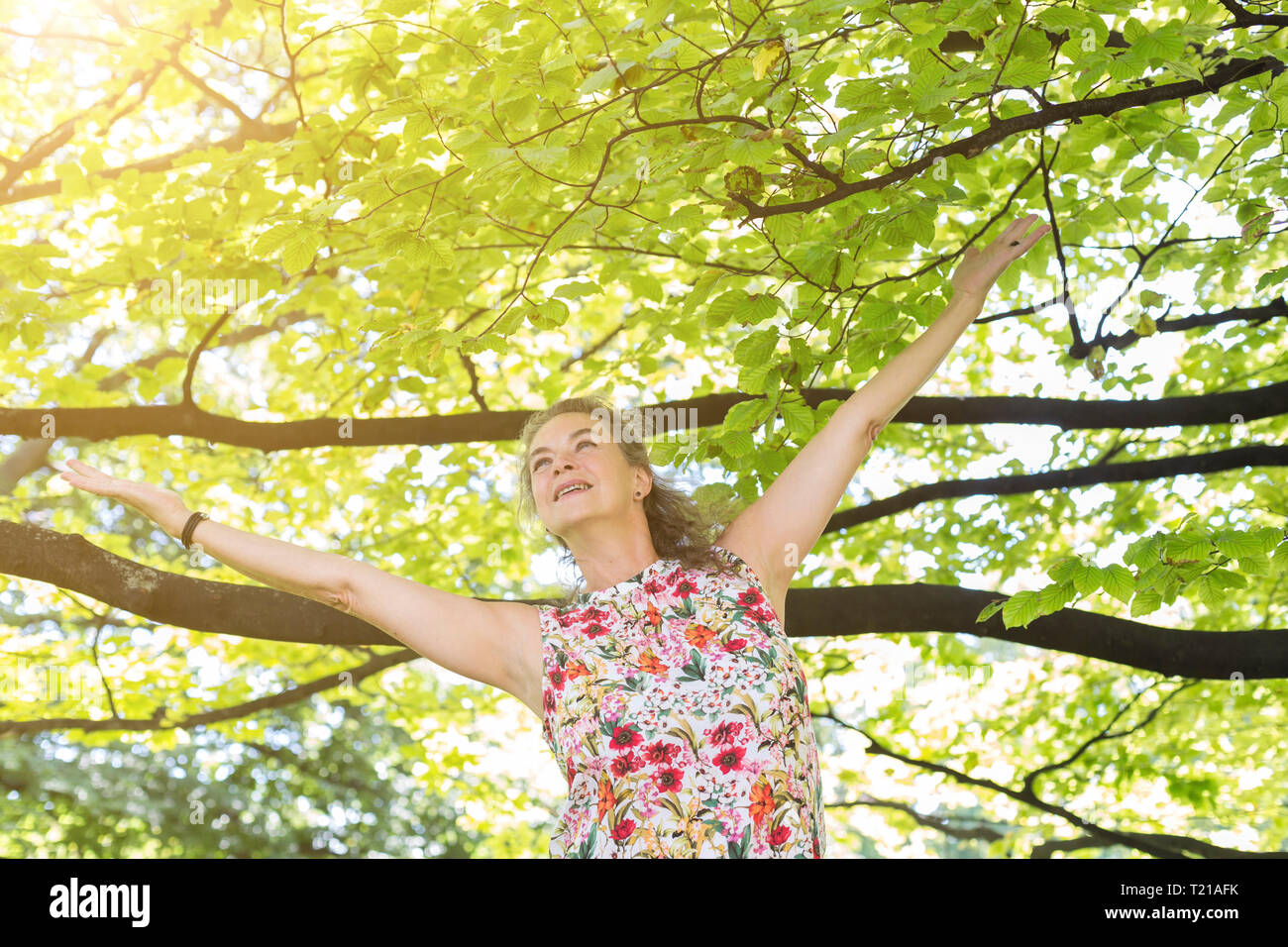 Sorridente donna matura indossare top con disegno floreale rilassante in un parco Foto Stock