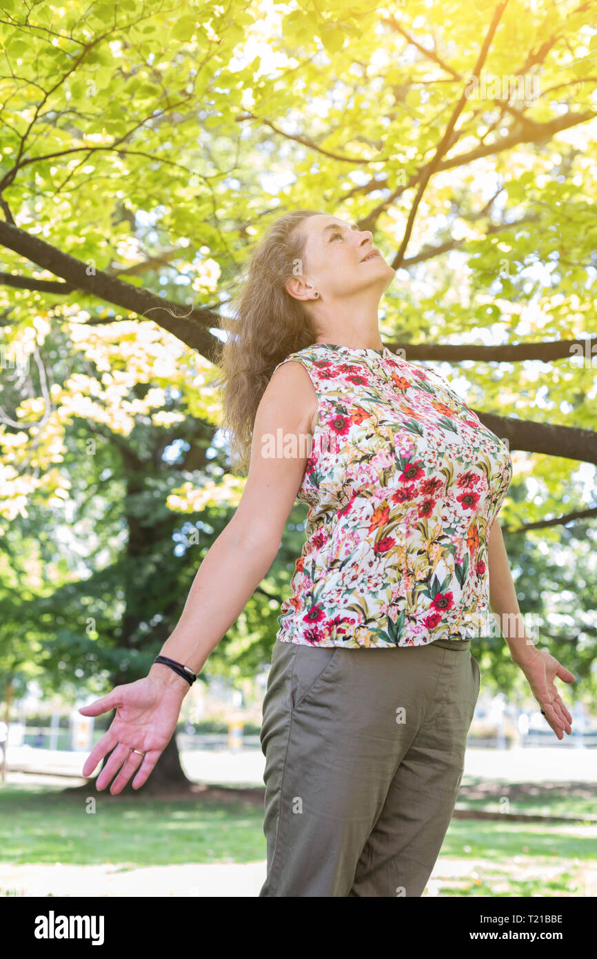Donna matura indossare top con disegno floreale rilassante in un parco Foto Stock