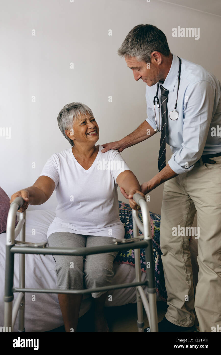 Medico maschio aiutando senior paziente femmina di camminare con walker Foto Stock