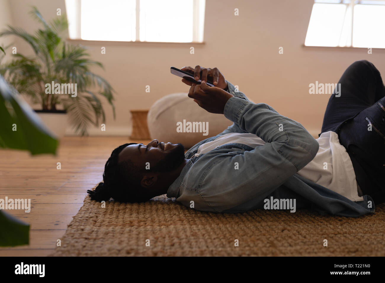 Uomo bello usando il cellulare mentre giacente sul piano a casa Foto Stock