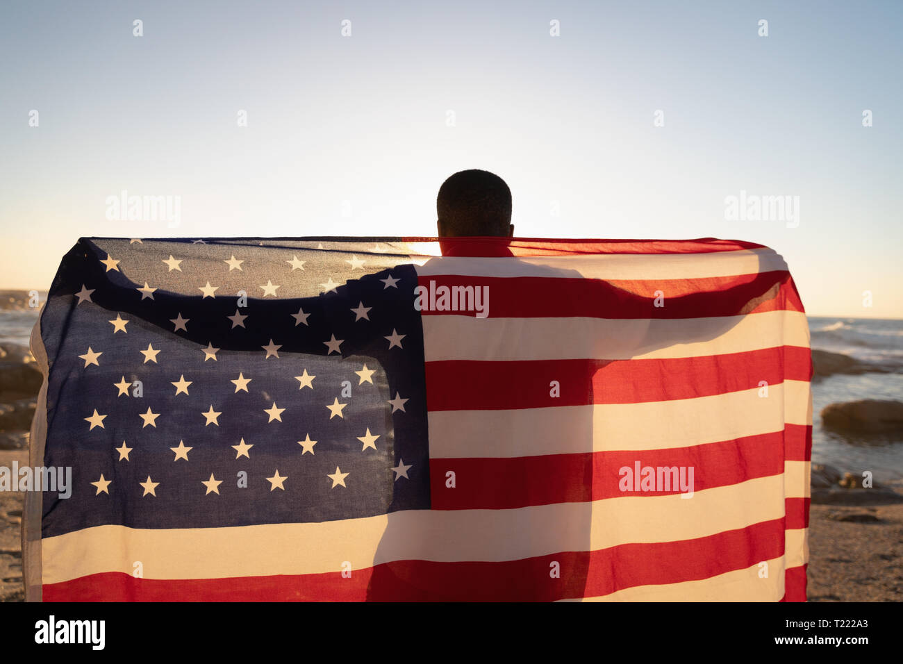 Uomo in piedi presso la spiaggia tenendo bandiera americana Foto Stock