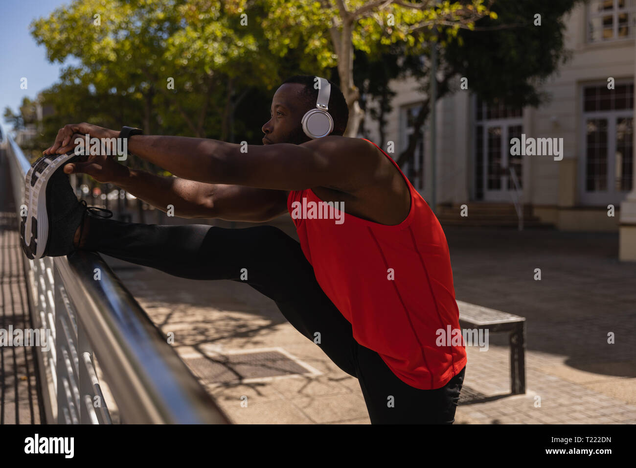 Uomo con cuffie gamba stretching contro la ringhiera sul lato a piedi Foto Stock
