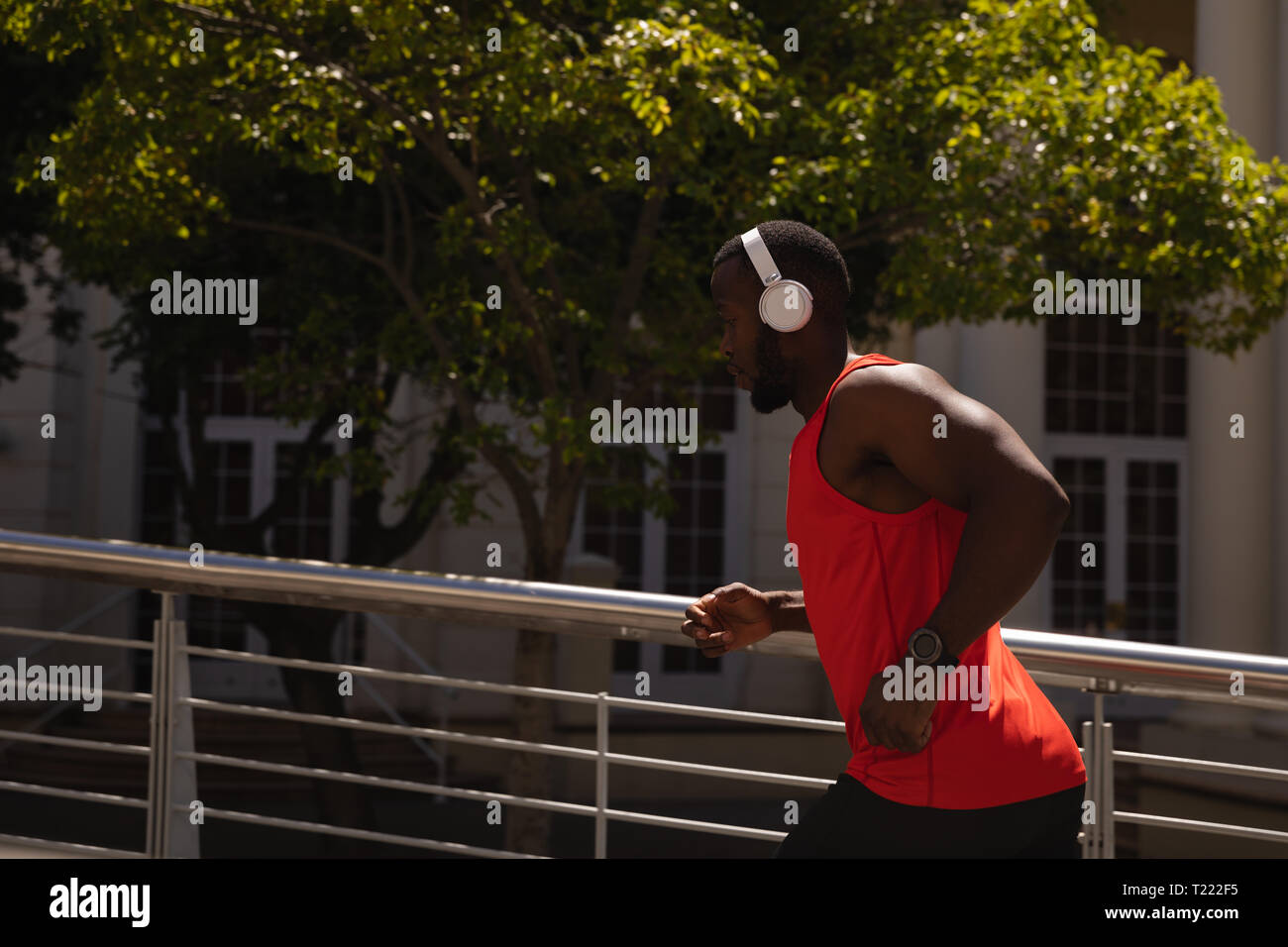 Uomo con cuffie in esecuzione contro la ringhiera in una giornata di sole Foto Stock