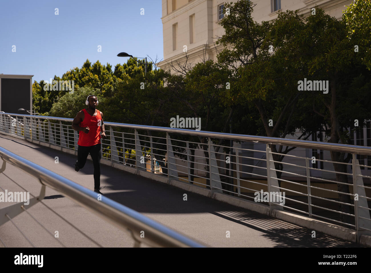 Uomo con cuffie in esecuzione contro la ringhiera in una giornata di sole Foto Stock