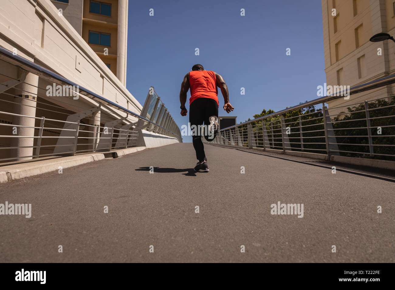 Uomo con cuffie in esecuzione contro la ringhiera in una giornata di sole Foto Stock