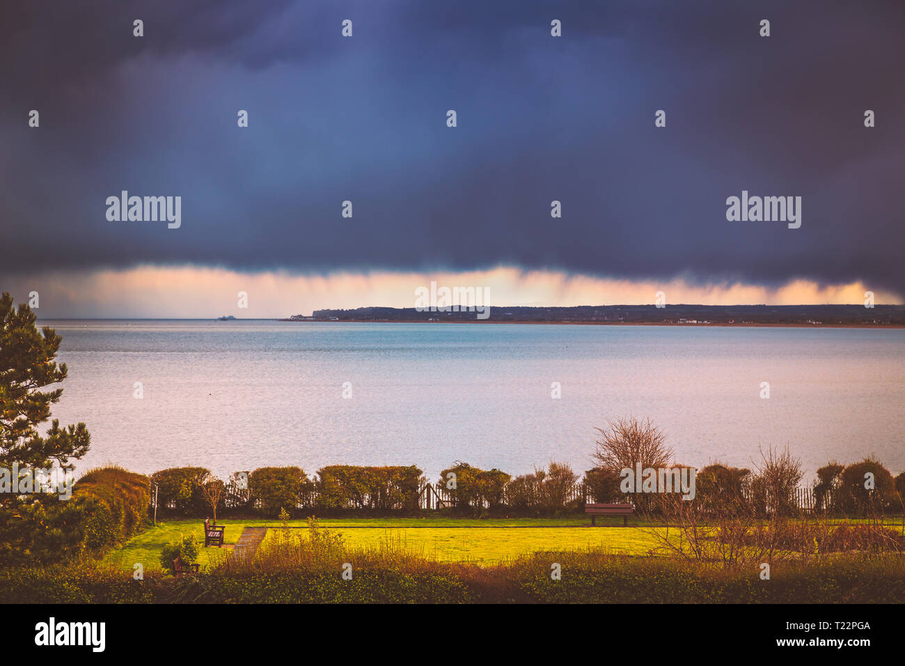 Heavy rainclouds oltre l'orizzonte e trattare e Sandwich nel Kent, Regno Unito mentre il sole su una zona del parco del Royal Esplanade, Ramsgate. Foto Stock