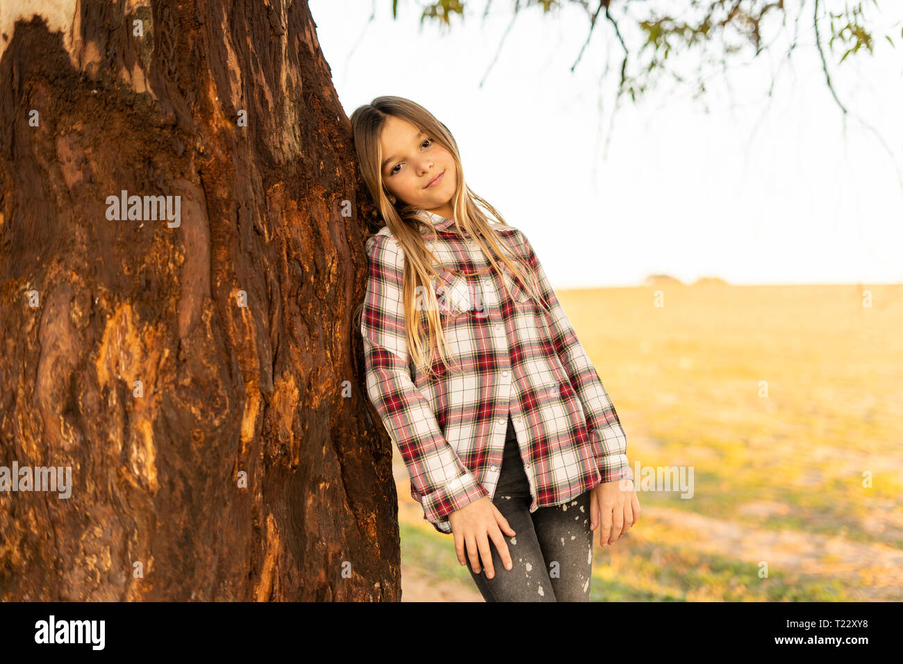 Ritratto di ragazza bionda appoggiata contro il tronco di albero Foto Stock