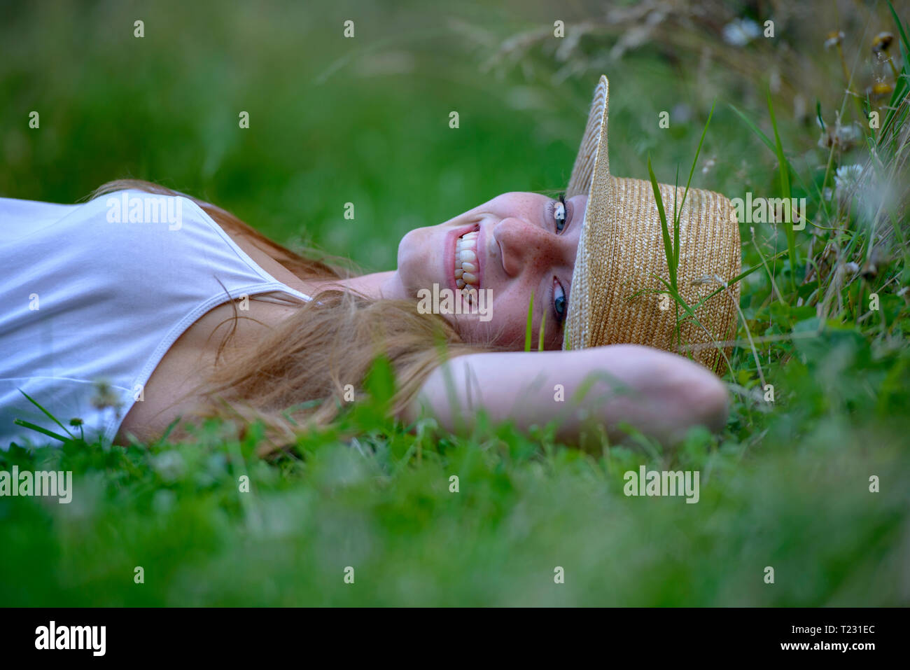 Ritratto di ridere ragazza adolescente indossando cappello di paglia sdraiati su un prato in estate Foto Stock