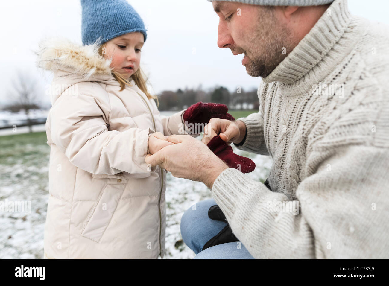 Padre aiutare mia figlia a mettere su guanti in inverno Foto Stock