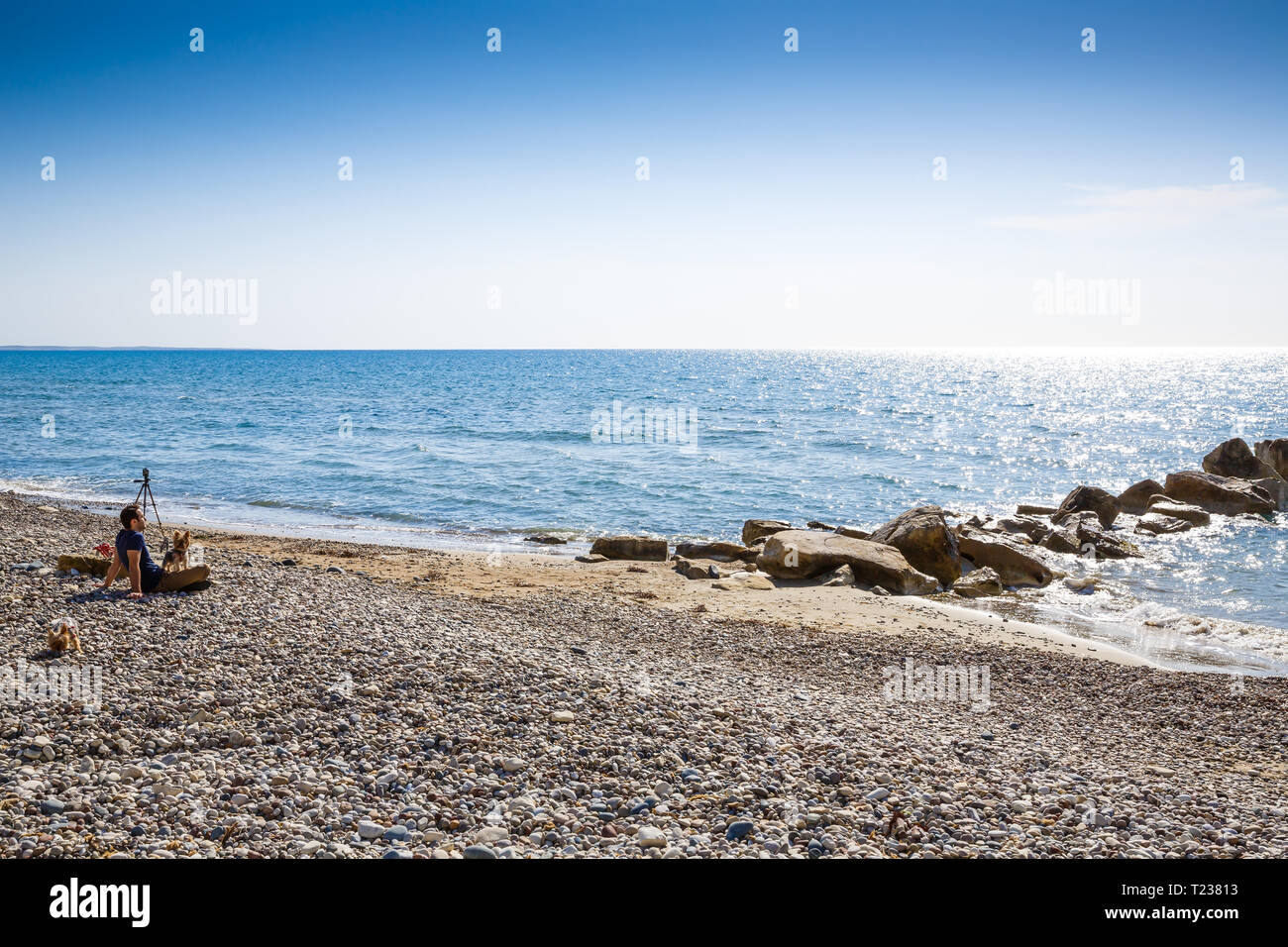 Blu mare Mediterraneo con la superficie di spumanti, pietre e l'uomo con i cani sulla spiaggia di Cipro. Foto Stock