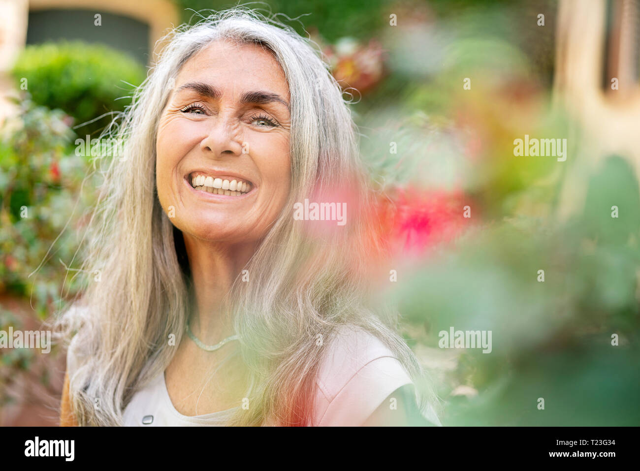 Ritratto di donna felice con lunghi capelli grigi in giardino Foto Stock