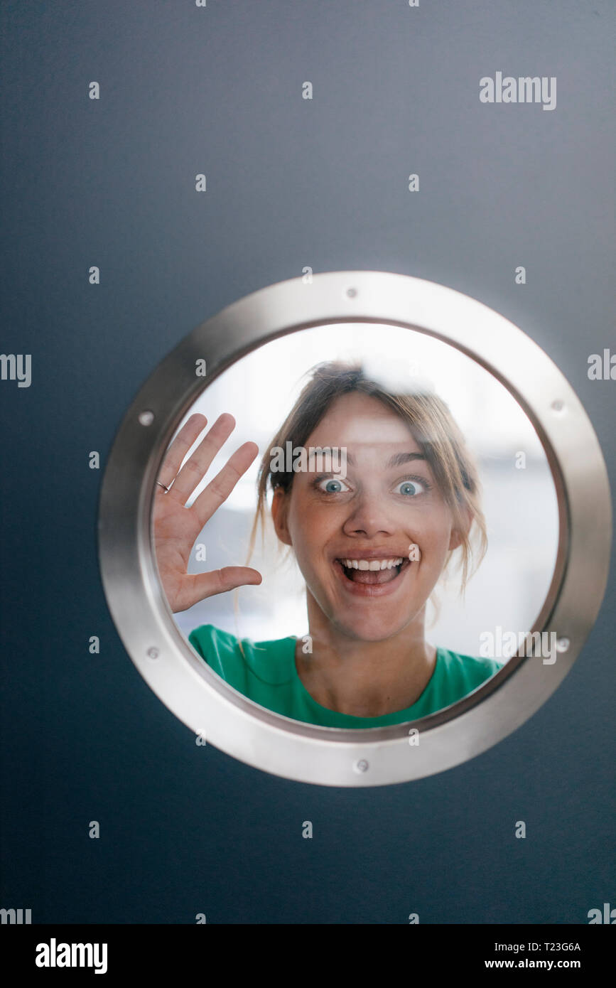 Ritratto di donna tirando facce buffe dietro oblò Foto Stock