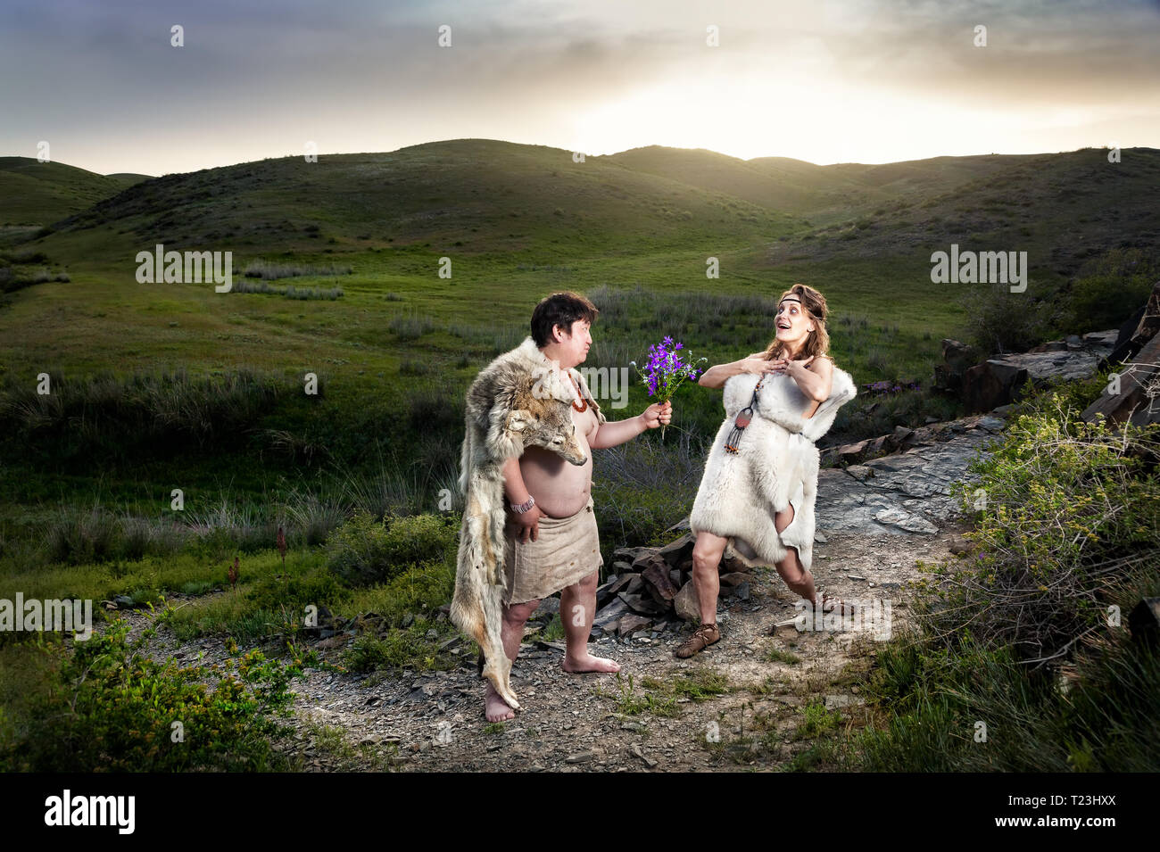 Primitiva caveman vestiti di pelle di animale dando ai fiori di grotta felice donna in montagna Foto Stock